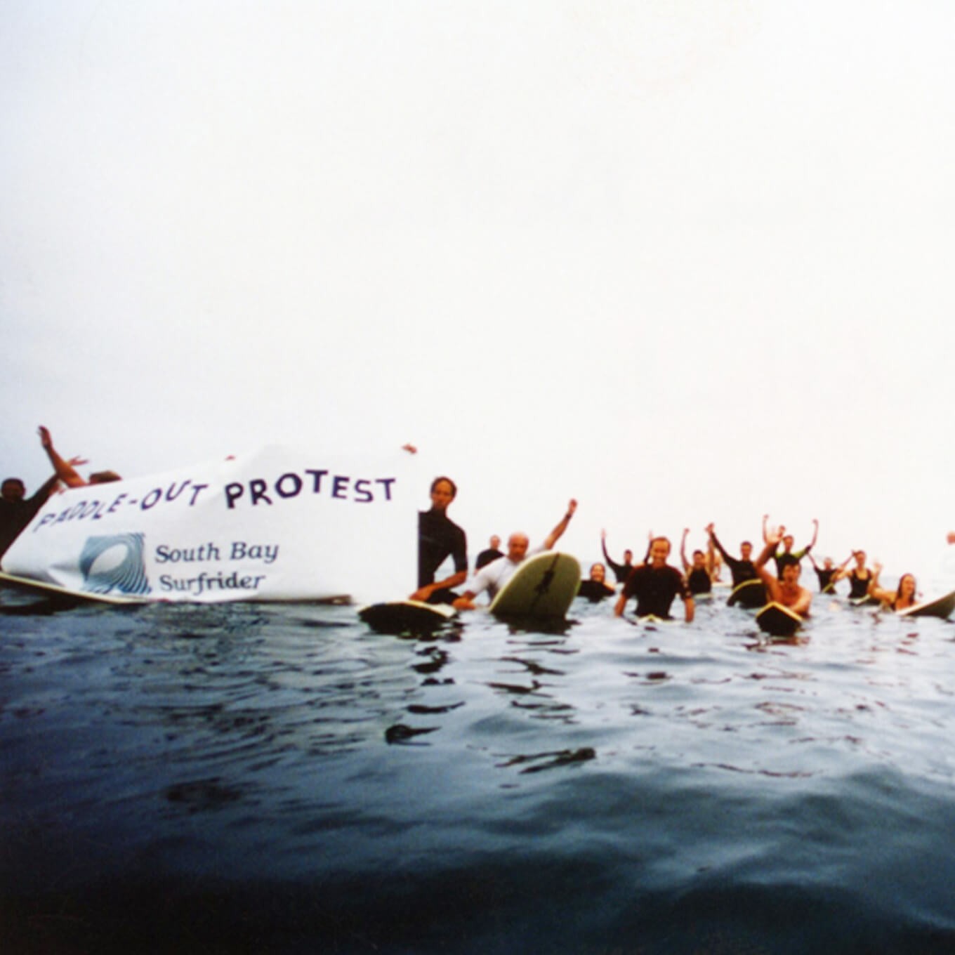 photo of Surfrider volunteers on surfboards floating in the ocean holding a Surfrider banner