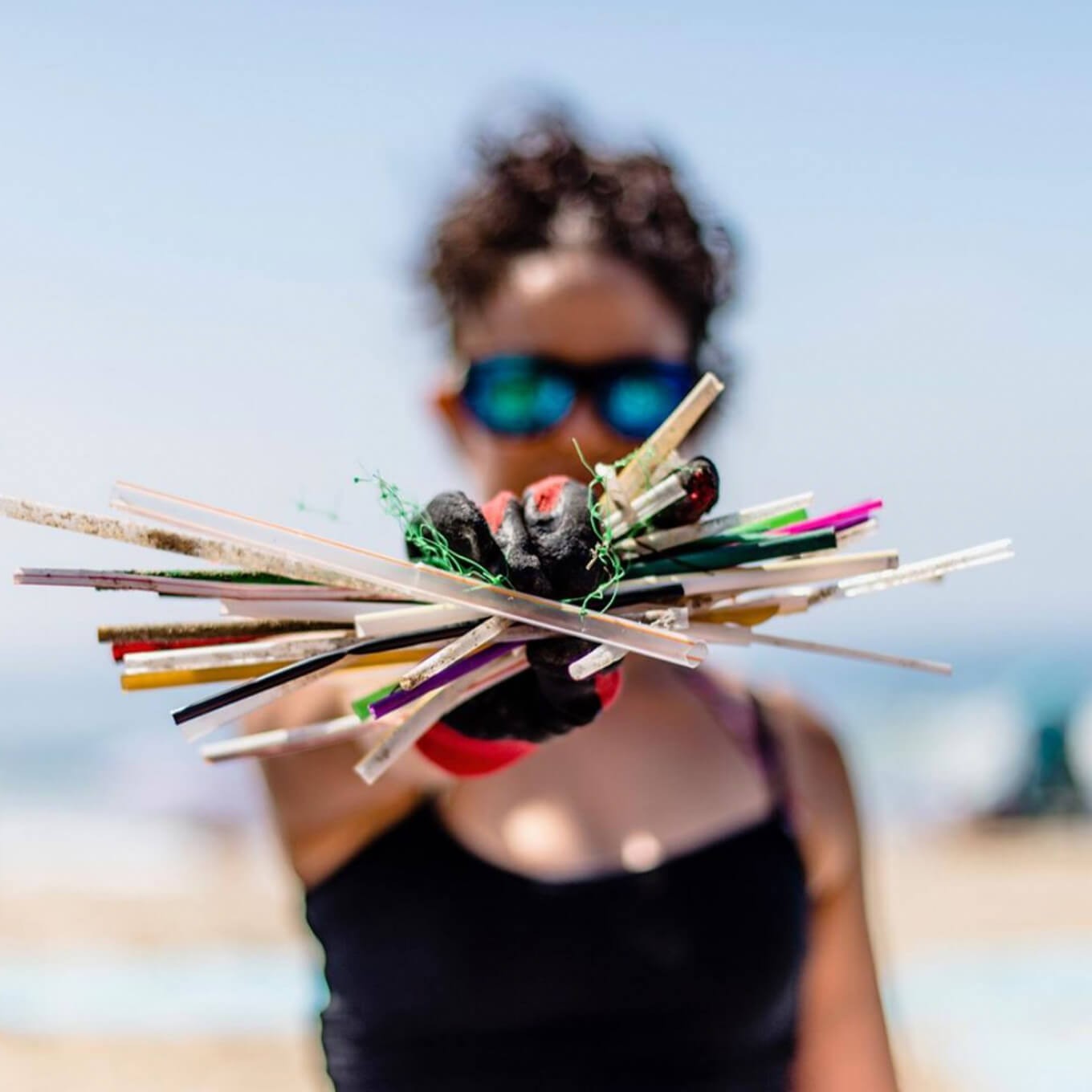 photo of a Surfrider volunteer holding straws that were collected at a beach cleanup